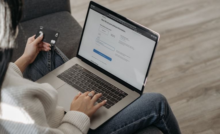 Person holding a credit card while shopping online on a laptop, representing ecommerce checkout and cart abandonment