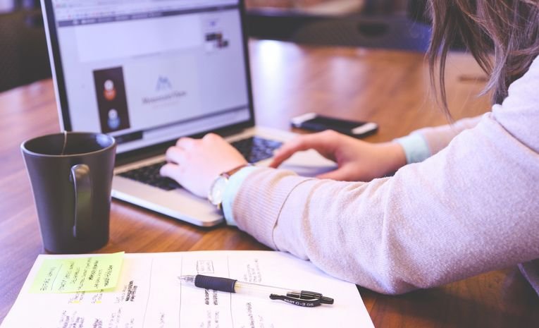 Businesswoman using a laptop with notes and coffee on a wooden desk, representing exploring startup funding and business support options