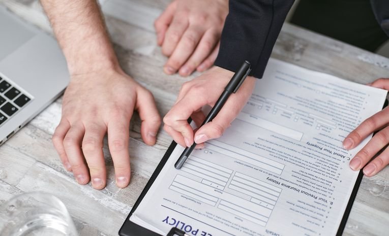 Two people signing an insurance policy document on a desk, representing different types of business insurance
